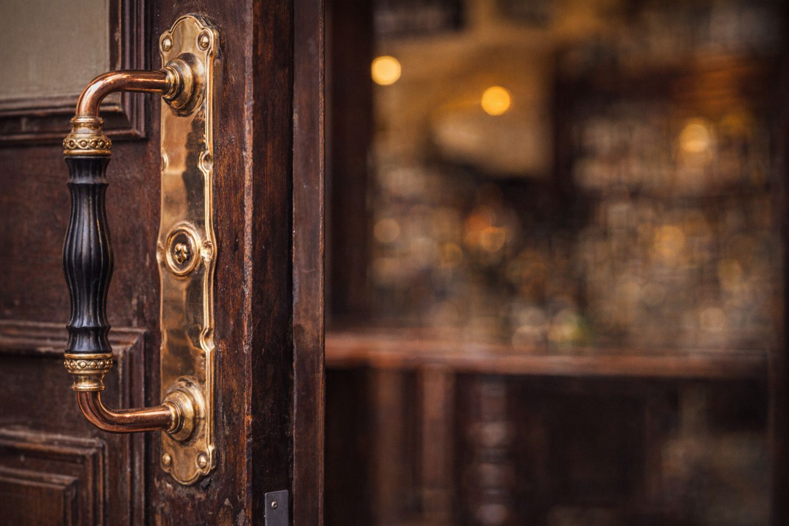 Een antieke koperen deurgreep op een donkere houten cafédeur.